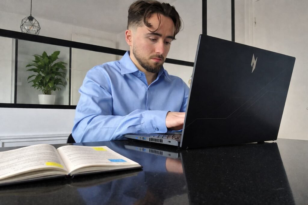 diététicien Mathis Bruguiere en consultation diététique en ligne en train de taper sur un ordinateur avec un carnet sur la table et une plante en arrière-plan